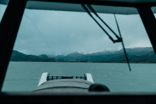 View of the glacial waters of Lago Argentino and distant snow capped Andes mountains seen through a boat windshield in El Calafate Santa Cruz Province Argentina.