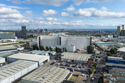 Aerial view of a large modern data center facility surrounded by industrial warehouses parking lots and urban infrastructure under a bright blue sky in the United Kingdom. Aerial view of a large modern data center facility surrounded by industrial warehouses parking lots and urban infrastructure under a bright blue sky in the United Kingdom.