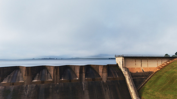 Aerial view of Midmar Dam featuring the concrete spillway calm water reservoir and grassy embankment under a misty sky in Howick KwaZulu Natal South Africa. Aerial view of Midmar Dam featuring the concrete spillway calm water reservoir and grassy embankment under a misty sky in Howick KwaZulu Natal South Africa.