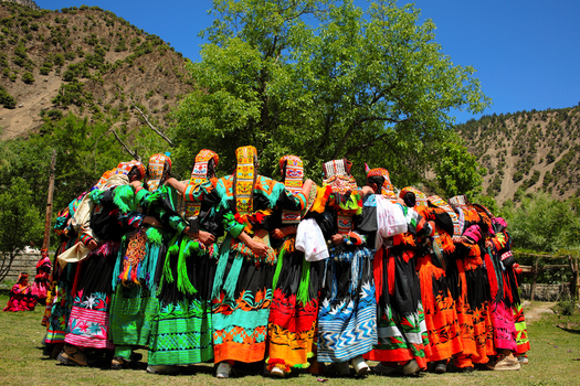 Chitral Khyber Pakhtunkhwa Pakistan 15 May 2013 View of women in traditional colorful Kalash dresses dancing in a circle in Rumbur valley with mountains in the background.