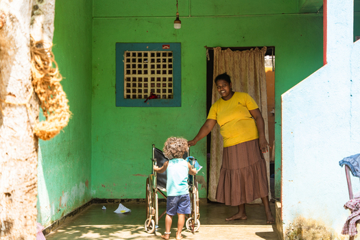 Sri Lanka 31 January 2026 View of a woman and a small child with a wheelchair on the porch of a bright green house.