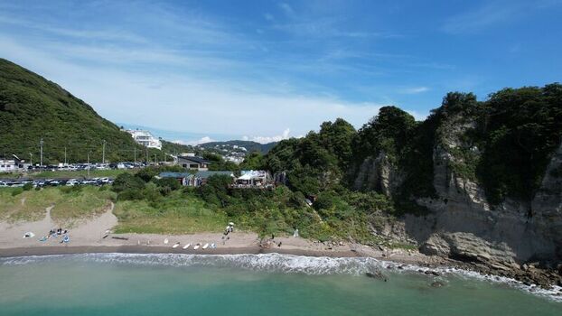 Aerial view of Chojagasaki cape featuring rocky cliffs a sandy beach lush greenery and coastal waters under a clear blue sky in Hayama Kanagawa Japan.
