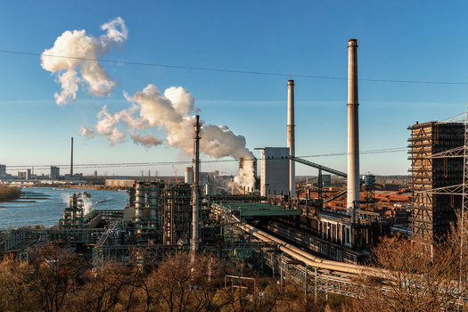 View of an industrial plant with smoking chimneys and steel structures along the Rhine river under a clear blue sky at sunset in Duisburg North Rhine Westphalia Germany.