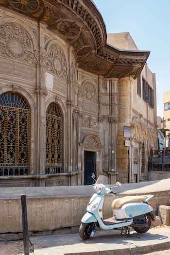 View of the Sabil Kuttab of Muhammad Ali Pasha featuring ornate stone carvings and arched windows with a light blue scooter parked on the street in Cairo Egypt. View of the Sabil Kuttab of Muhammad Ali Pasha featuring ornate stone carvings and arched windows with a light blue scooter parked on the street in Cairo Egypt.