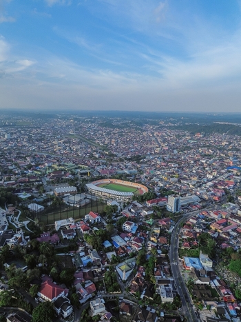 Aerial view of Segiri Stadium surrounded by dense urban rooftops and city infrastructure in Samarinda East Kalimantan Indonesia.