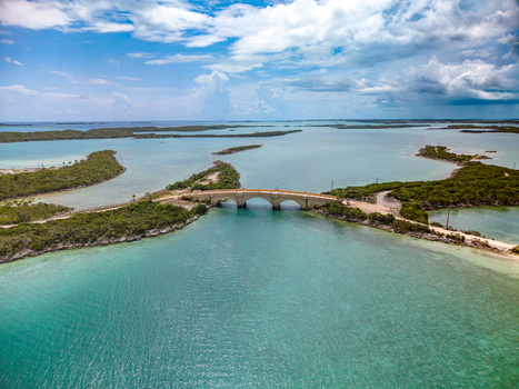 Aerial view of the stone bridge at Crab Cay connecting lush green islands over turquoise tropical waters under a cloudy sky in Exuma Exuma The Bahamas. Aerial view of the stone bridge at Crab Cay connecting lush green islands over turquoise tropical waters under a cloudy sky in Exuma Exuma The Bahamas.