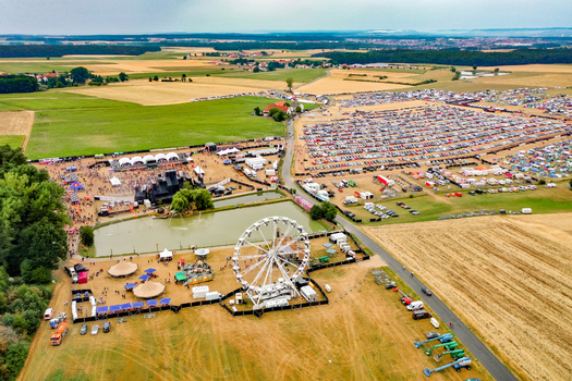 Herzogenaurach Germany 22 July 2022 Aerial view of the Open Beatz Festival featuring a Ferris wheel multiple stages and large crowds of people surrounded by agricultural fields. Herzogenaurach Germany 22 July 2022 Aerial view of the Open Beatz Festival featuring a Ferris wheel multiple stages and large crowds of people surrounded by agricultural fields.