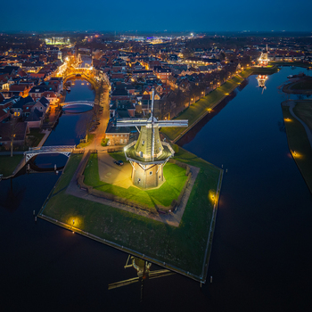 Aerial view of the illuminated De Hoop windmill on a green bastion surrounded by calm canal waters and city lights at night in Dokkum Friesland Netherlands. Aerial view of the illuminated De Hoop windmill on a green bastion surrounded by calm canal waters and city lights at night in Dokkum Friesland Netherlands.