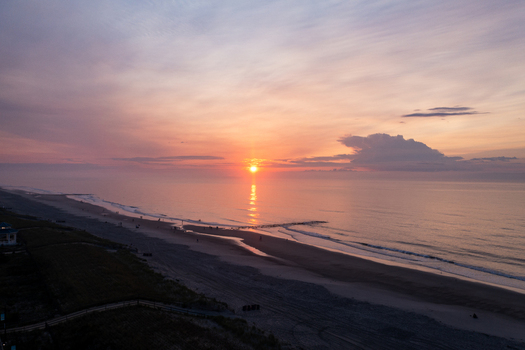Aerial view of Sea Isle City Beach at sunrise with calm waves golden light reflecting on the water and a soft pink sky in Sea Isle City New Jersey United States.