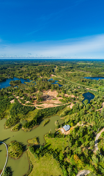 Aerial view of a house nestled among lush green forests and serene lakes under a clear blue sky in Latvia. Aerial view of a house nestled among lush green forests and serene lakes under a clear blue sky in Latvia.