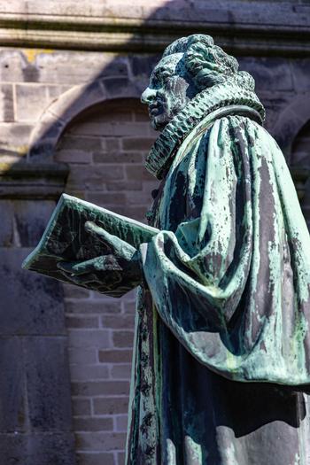View of the Hans Tausen statue holding a book in front of the historic Ribe Cathedral with its stone arches and weathered walls in Ribe Denmark. View of the Hans Tausen statue holding a book in front of the historic Ribe Cathedral with its stone arches and weathered walls in Ribe Denmark.