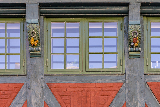 View of traditional half timbered house facade featuring green windows ornate carved wooden corbels with fruit motifs and red brickwork in Ribe Denmark. View of traditional half timbered house facade featuring green windows ornate carved wooden corbels with fruit motifs and red brickwork in Ribe Denmark.