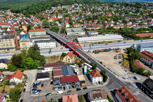 Aerial view of Piastenbrucke with its distinctive red arches crossing over railway tracks surrounded by urban buildings and lush green trees in Forchheim Bayern Germany.