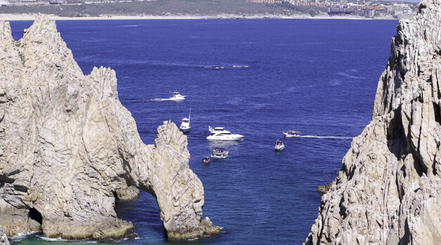 Aerial view of the iconic El Arco rock formation surrounded by turquoise waters with several boats navigating the bay in Cabo San Lucas Baja California Sur Mexico.