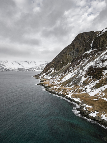 Aerial view of Grotfjord with steep rocky cliffs snow covered slopes and deep blue water under a cloudy sky Tromvik Troms Norway. Aerial view of Grotfjord with steep rocky cliffs snow covered slopes and deep blue water under a cloudy sky Tromvik Troms Norway.