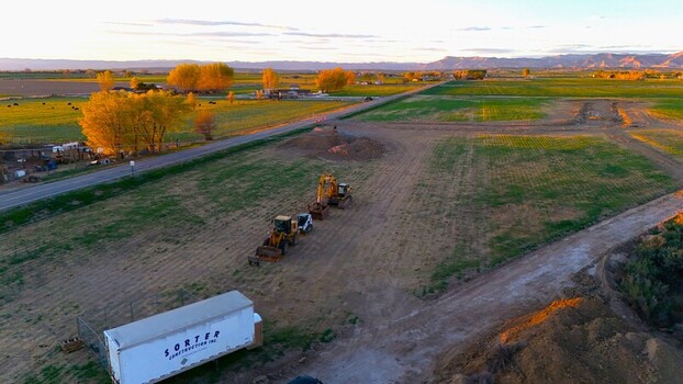 Aerial view of construction machinery and earthworks on a rural development site surrounded by green fields and distant mountains during golden hour Loma Colorado United States. Aerial view of construction machinery and earthworks on a rural development site surrounded by green fields and distant mountains during golden hour Loma Colorado United States.