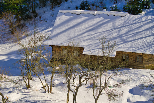 View of a rustic wooden cabin nestled amidst a snow covered landscape with bare trees reaching towards a winter sky Moce Banska Bystrica Region Slovakia.