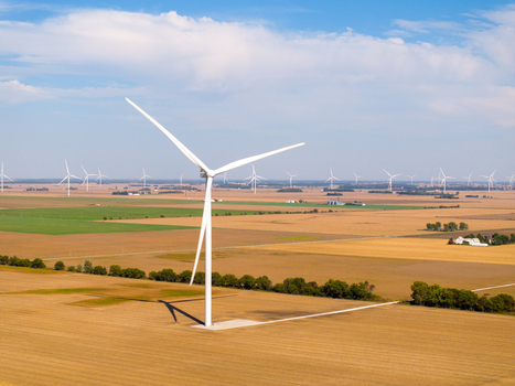 Aerial view of wind turbines in a large wind farm set against golden agricultural fields under a clear blue sky in Wolcott Indiana United States.