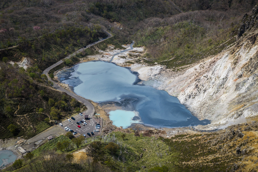 Aerial view of the volcanic Oyunuma Pond with its steaming sulfurous water surrounded by rugged terrain forest and a parking area in Noboribetsu Hokkaido Japan. Aerial view of the volcanic Oyunuma Pond with its steaming sulfurous water surrounded by rugged terrain forest and a parking area in Noboribetsu Hokkaido Japan.