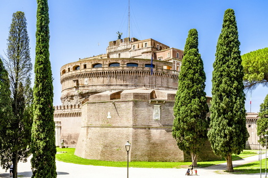 View of the historic Castel Sant Angelo with its cylindrical brick walls framed by tall cypress trees under a clear blue sky in Rome Lazio Italy. View of the historic Castel Sant Angelo with its cylindrical brick walls framed by tall cypress trees under a clear blue sky in Rome Lazio Italy.