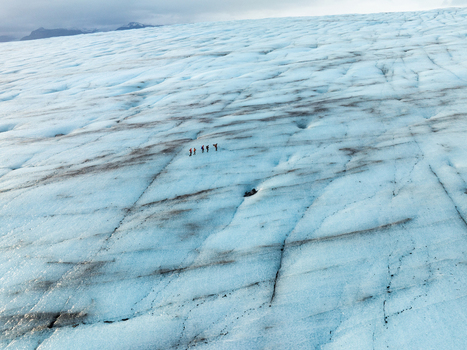Aerial view of Breidamerkurjokull glacier with hikers walking across the blue ice and black volcanic ash streaks in Sveitarfelagid Hornafjordur Iceland. Aerial view of Breidamerkurjokull glacier with hikers walking across the blue ice and black volcanic ash streaks in Sveitarfelagid Hornafjordur Iceland.