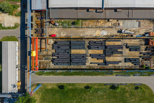 Aerial view of an industrial storage yard featuring neatly stacked metal pipes a large overhead gantry crane and surrounding facility buildings in Kyjov South Moravian Region Czechia.