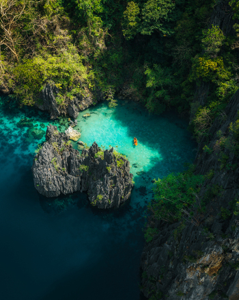 Aerial view of Big Lagoon with turquoise waters towering limestone cliffs and a small kayak paddling through the lagoon in El Nido Bay Philippines. Aerial view of Big Lagoon with turquoise waters towering limestone cliffs and a small kayak paddling through the lagoon in El Nido Bay Philippines.