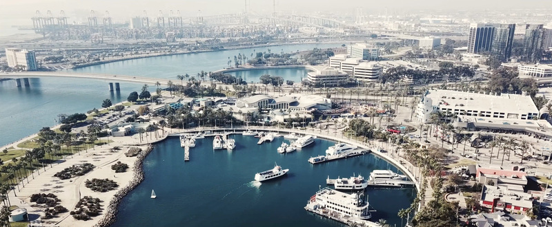 Aerial view of Rainbow Harbor with boats docked at the marina surrounded by palm trees and modern buildings in Long Beach California United States.