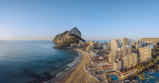 Aerial view of the iconic Penon de Ifach rock formation rising above the Mediterranean coastline sandy beach and modern apartment buildings in Calp Valencian Community Spain. Aerial view of the iconic Penon de Ifach rock formation rising above the Mediterranean coastline sandy beach and modern apartment buildings in Calp Valencian Community Spain.