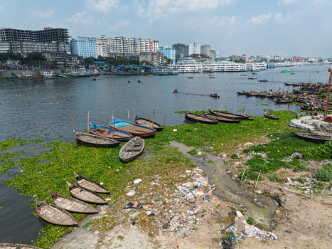 Aerial view of Buriganga River with wooden boats moored near the shore and the city skyline in Dhaka Dhaka Division Bangladesh.