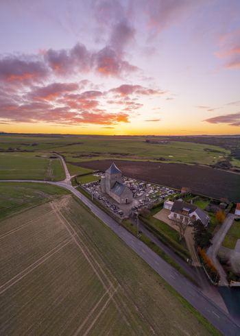 Aerial view of the Saint Jean Baptiste church surrounded by a cemetery and rural fields during a vibrant sunset in Audresselles Hauts de France France.