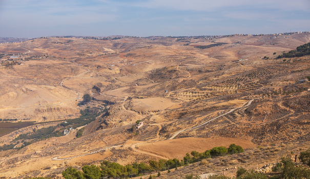 Aerial view of the arid hilly landscape surrounding Mount Nebo featuring winding dirt roads and sparse vegetation in Faisaliah Sub District Madaba Governorate Jordan. Aerial view of the arid hilly landscape surrounding Mount Nebo featuring winding dirt roads and sparse vegetation in Faisaliah Sub District Madaba Governorate Jordan.