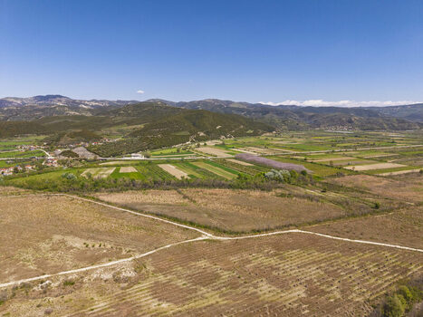 Aerial view of Vjosa Wild River National Park featuring lush green agricultural fields rolling hills and a clear blue sky in the rural landscape of Permet Gjirokaster County Albania. Aerial view of Vjosa Wild River National Park featuring lush green agricultural fields rolling hills and a clear blue sky in the rural landscape of Permet Gjirokaster County Albania.