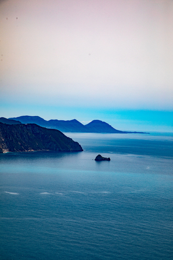 Aerial view of the rugged coastline and turquoise waters of the Ionian Sea with distant mountains and a small rocky islet near Corfu Ionian Islands Greece. Aerial view of the rugged coastline and turquoise waters of the Ionian Sea with distant mountains and a small rocky islet near Corfu Ionian Islands Greece.