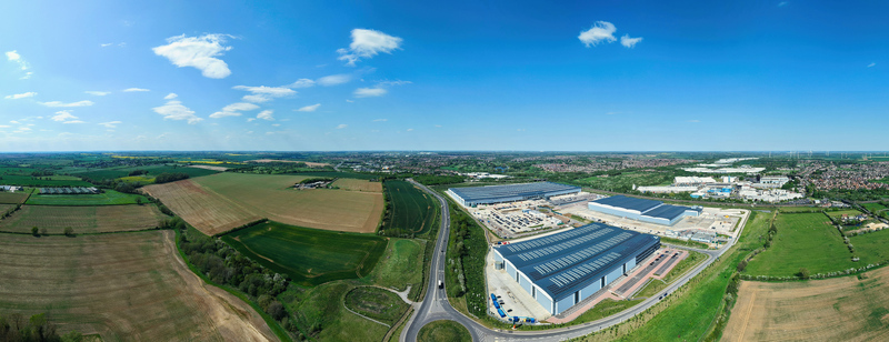 Aerial view of Symmetry Park logistics hub featuring large modern warehouses surrounded by green agricultural fields and a road junction in Kettering England United Kingdom. Aerial view of Symmetry Park logistics hub featuring large modern warehouses surrounded by green agricultural fields and a road junction in Kettering England United Kingdom.