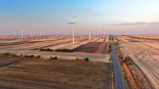 Aerial view of a wind farm with multiple turbines set amidst vast agricultural fields and a straight road stretching into the horizon in Vladimirovac Vojvodina Serbia.