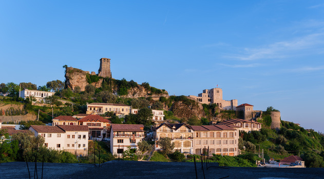 View of the historic Kruje Castle and Skanderbeg Museum perched on a rocky hillside with traditional houses under a clear blue sky in Kruje Durres County Albania.