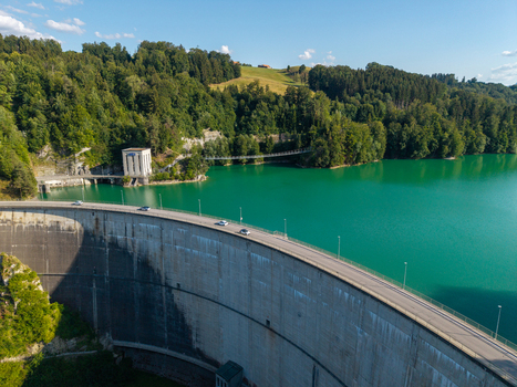 Aerial view of Barrage de Rossens dam wall with cars driving along the road turquoise water of Lac de la Gruyere and lush green forest in Pont la Ville Fribourg Switzerland.