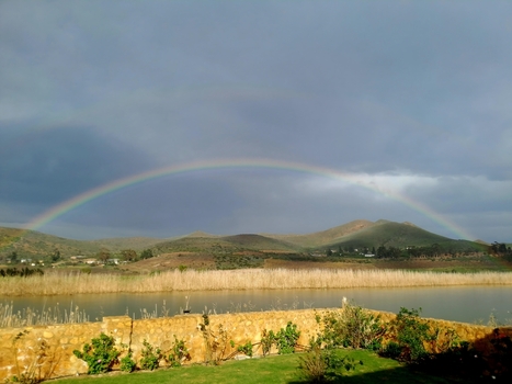 View of a vibrant rainbow arching over a tranquil pond and rolling mountains in Montagu Western Cape South Africa.