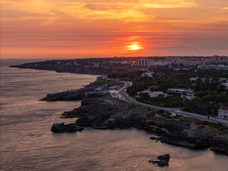 Aerial view of the rocky coastline at Boca do Inferno during a vibrant sunset with the coastal road and buildings of Cascais Lisboa Portugal. Aerial view of the rocky coastline at Boca do Inferno during a vibrant sunset with the coastal road and buildings of Cascais Lisboa Portugal.