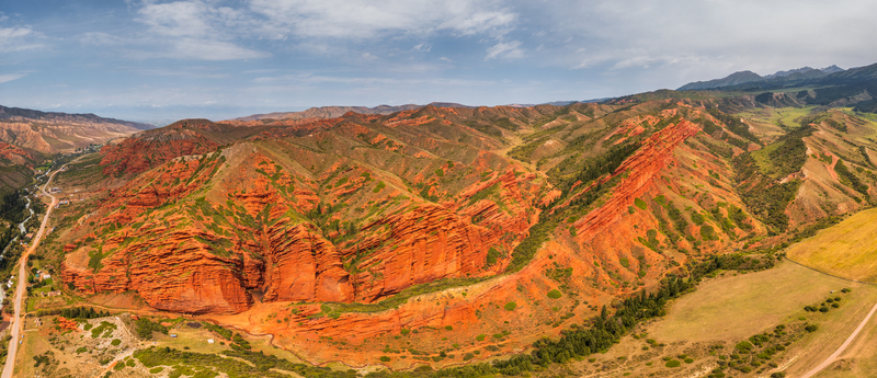 Aerial view of the iconic Seven Bulls Rock red sandstone formations surrounded by lush green slopes and rugged mountain terrain in Dzhetyoguz Issyk Kul Region Kyrgyzstan.