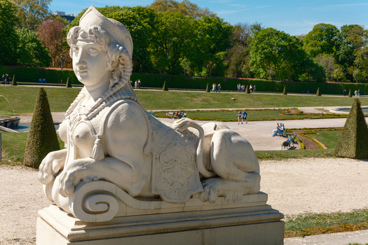 View of a white stone sphinx statue in the gardens of Belvedere Palace with manicured lawns and people in Vienna Vienna Austria. View of a white stone sphinx statue in the gardens of Belvedere Palace with manicured lawns and people in Vienna Vienna Austria.