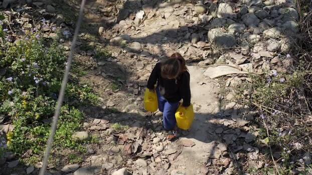 View of a girl carrying water containers on a rocky path Nepal.