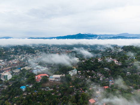 Aerial view of the urban landscape of Kandy nestled among lush green hills and covered by thick white mist under an overcast sky Kandy Central Province Sri Lanka. Aerial view of the urban landscape of Kandy nestled among lush green hills and covered by thick white mist under an overcast sky Kandy Central Province Sri Lanka.