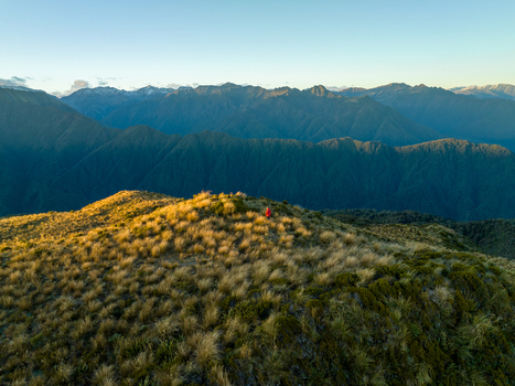 Aerial view of golden hour light kissing the grassy peaks contrasting with the deep blue of distant mountains Lake Kaniere West Coast Region New Zealand. Aerial view of golden hour light kissing the grassy peaks contrasting with the deep blue of distant mountains Lake Kaniere West Coast Region New Zealand.