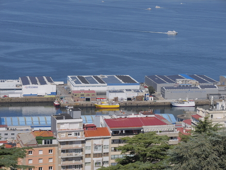 View of the industrial port area of Vigo with fishing boats docked at the quay warehouses with solar panels on rooftops and urban buildings in the foreground Vigo Pontevedra Spain.