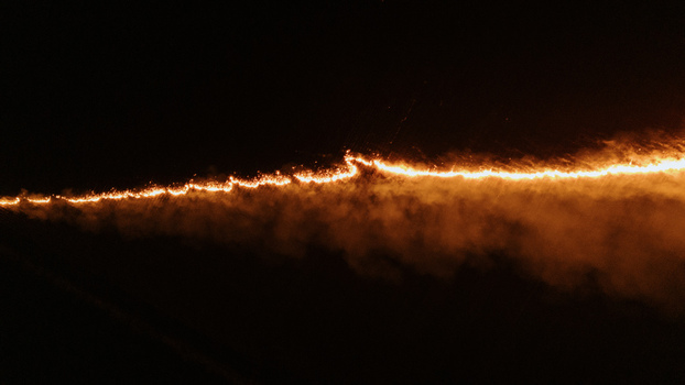 Aerial view of a long line of fire burning across a dark field at night in Sremska Mitrovica Vojvodina Serbia.
