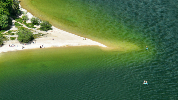 Aerial view of the sandy beach meeting the serene waters of Lac de Joux creating a tranquil oasis under the sun Le Lieu Vaud Switzerland.