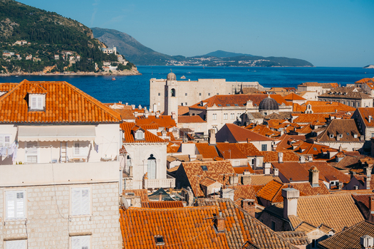 View of red tiled rooftops of the historic old town overlooking the Adriatic Sea and lush green hills under a clear blue sky Dubrovnik Dubrovnik Neretva County Croatia. View of red tiled rooftops of the historic old town overlooking the Adriatic Sea and lush green hills under a clear blue sky Dubrovnik Dubrovnik Neretva County Croatia.