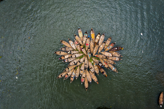 Aerial view of a cluster of wooden boats arranged in a circular pattern on the river water in Dhaka Dhaka Division Bangladesh.